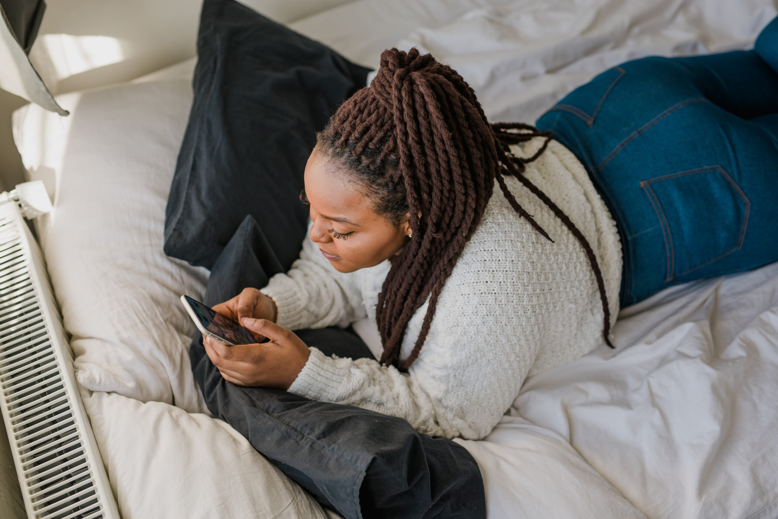 Woman lying on bed using smartphone, representing someone checking social media.